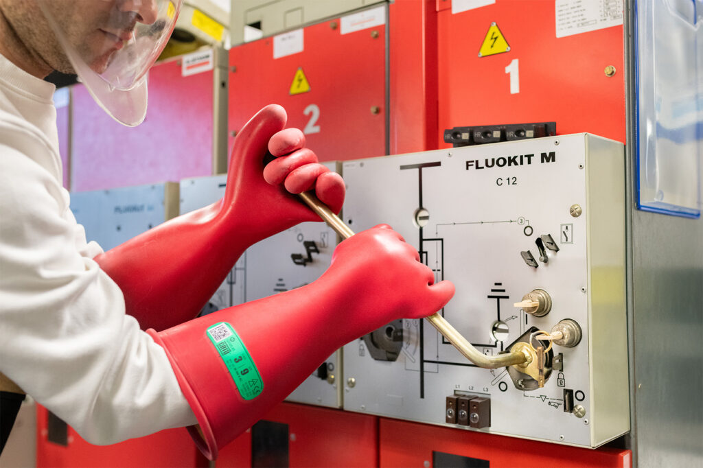 Opérateur en habilitation électrique HTA manipulant un sectionneur sur un tableau électrique FLUOKIT M avec des gants isolants haute tension