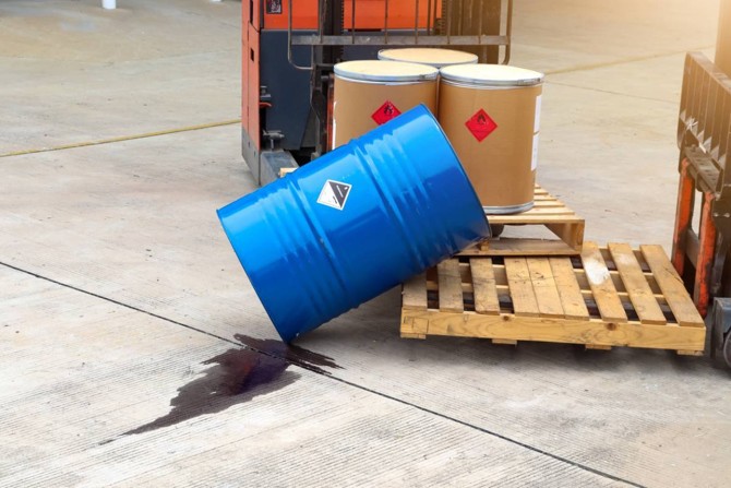 Fût bleu de produit chimique renversé au sol, fuite de liquide sur une zone de stockage industrielle.